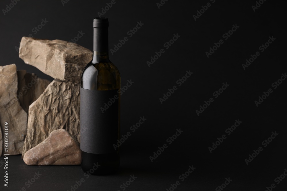 Naklejka premium Bottle of wine and rocks on black background, space for text