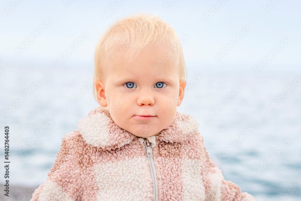 A delightful and charming toddler is gazing intently at the camera, set against a beautiful scenic water backdrop