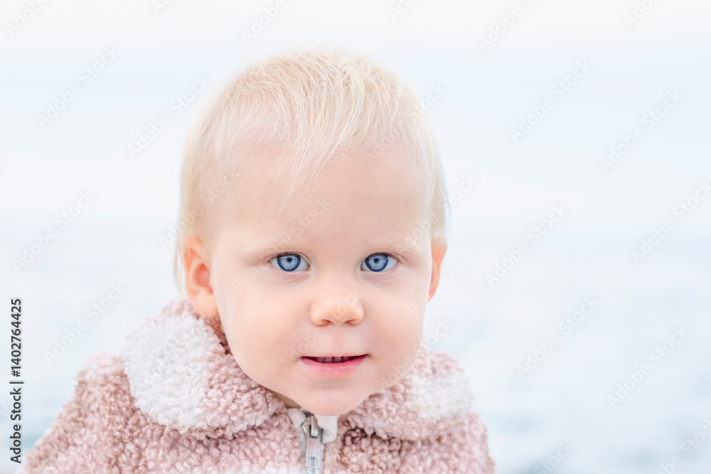 A delightful and charming toddler is gazing intently at the camera, set against a beautiful scenic water backdrop