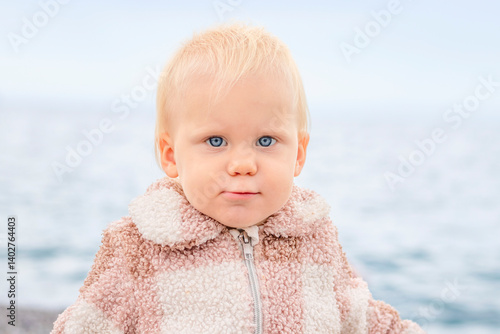Obraz na płótnie A delightful and charming toddler is gazing intently at the camera, set against a beautiful scenic water backdrop w salonie