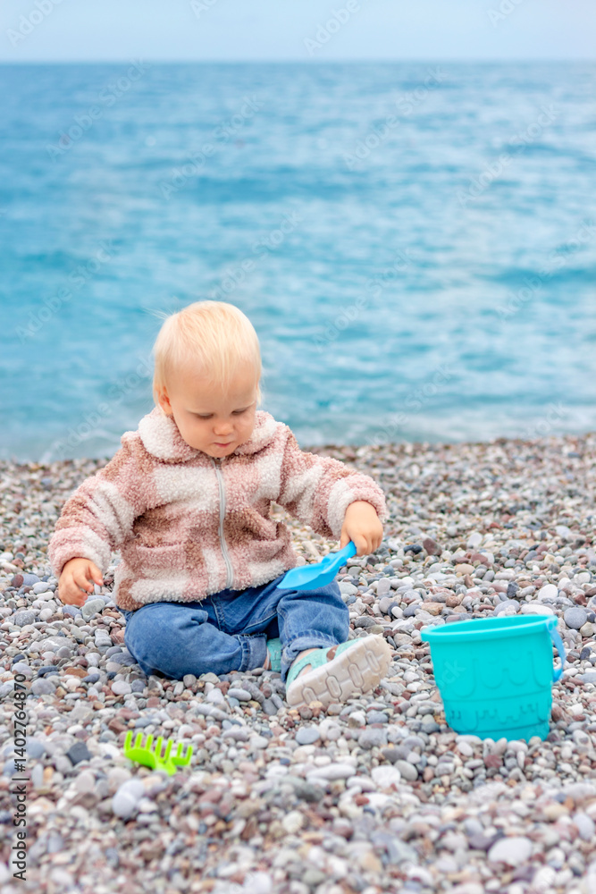A young child happily explores a rocky beach, playing with colorful toys while enjoying the beautiful sea view