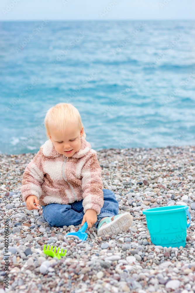 A young child happily explores a rocky beach, playing with colorful toys while enjoying the beautiful sea view