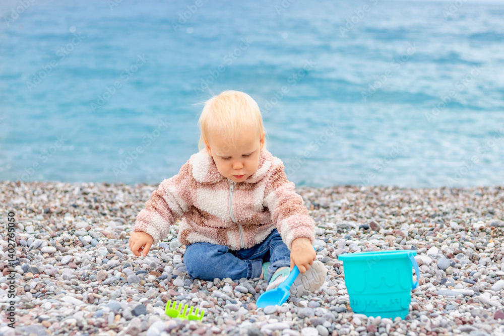A young child happily explores a rocky beach, playing with colorful toys while enjoying the beautiful sea view