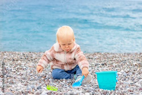 Obraz na płótnie A young child happily explores a rocky beach, playing with colorful toys while enjoying the beautiful sea view w salonie