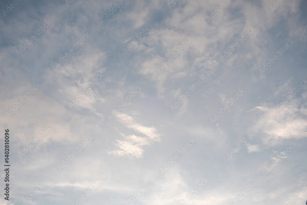 Fototapeta premium Wispy cirrus clouds scatter across a soft blue sky in the early morning, creating a light, airy backdrop with a calm and peaceful atmosphere.
