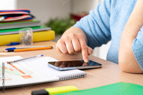 Bored student surfing the online and holding a smartphone on a desk at home.