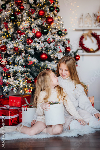Two cute sisters at the christmas tree with gifts