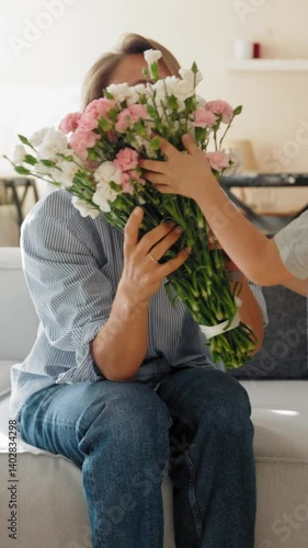 Young boy gives his mother a bouquet of flowers at home in a warm and cozy setting. She smiles with joy and gratitude. Concept of Mother's Day celebration and family love. Mid-range shot natural light