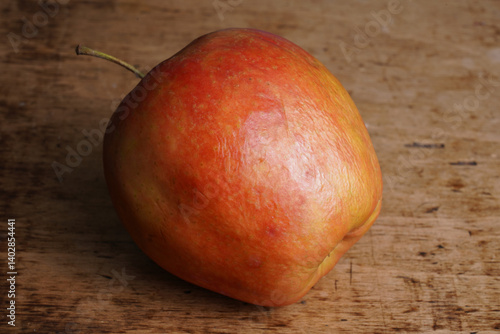 Bright red apple resting on wooden surface in natural light