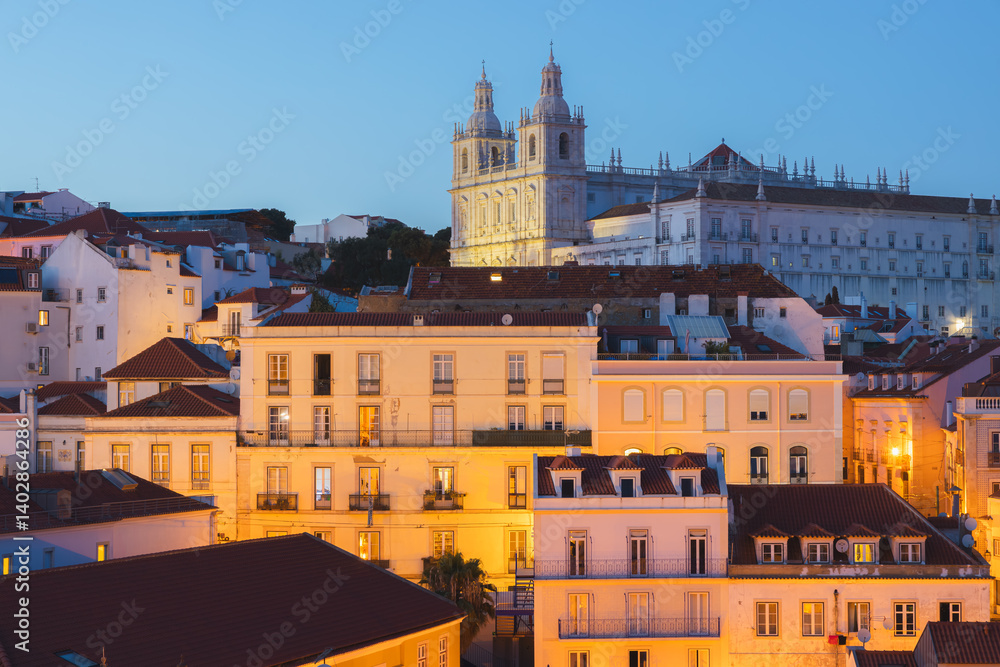 A cityscape view of Lisbon’s historic district from Miradouro de Santa Luzia, of the Church of St. Vincent de Fora at twilight in Lisbon, Portugal. A cityscape view of Lisbon’s historic district from Miradouro de Santa Luzia, of the Church of St. Vincent de Fora at twilight in Lisbon, Portugal.