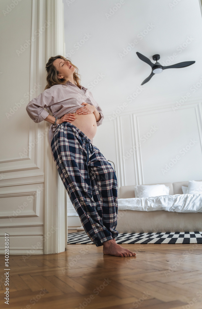 Pregnant happy woman with hands on belly stomach standing in apartment