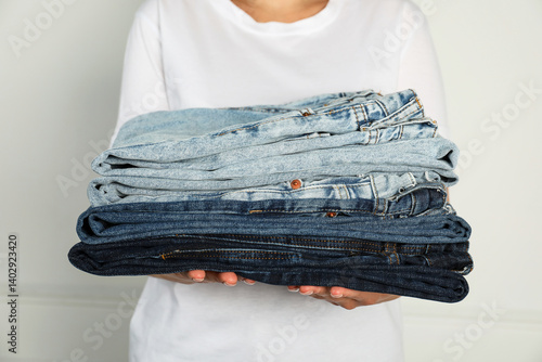 Obraz na płótnie Woman with stack of different stylish jeans near light wall indoors, closeup w salonie