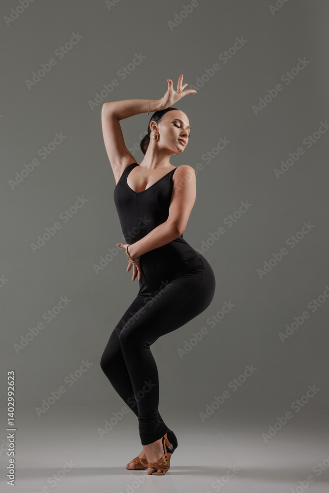 Stylish dancer posing in black bodysuit with expressive posture on gray background. Stylish dancer posing in black bodysuit with expressive posture on gray background.