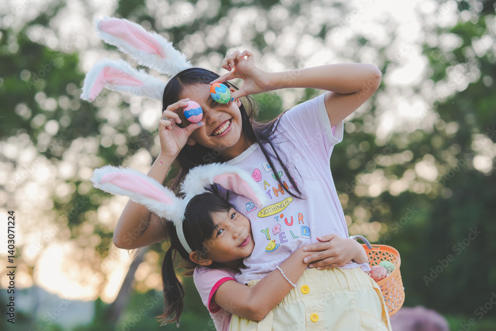Obraz premium Two girls have fun finding Easter eggs a favorite activity for all kids. The girls wear cute bunny ears on the head holding a basket with Easter eggs in a natural garden with evening light.