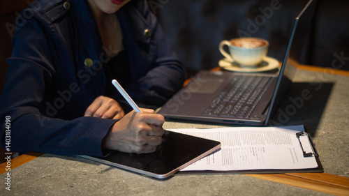 Wallpaper Mural A businesswoman is intently writing something on a tablet placed on a checklist, using a white touchscreen pen, and working on a laptop in a cozy corner of a cafe. Torontodigital.ca