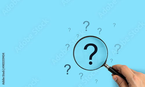 Fotografie Focusing on a large question mark, A hand holding a magnifying glass over a larg
