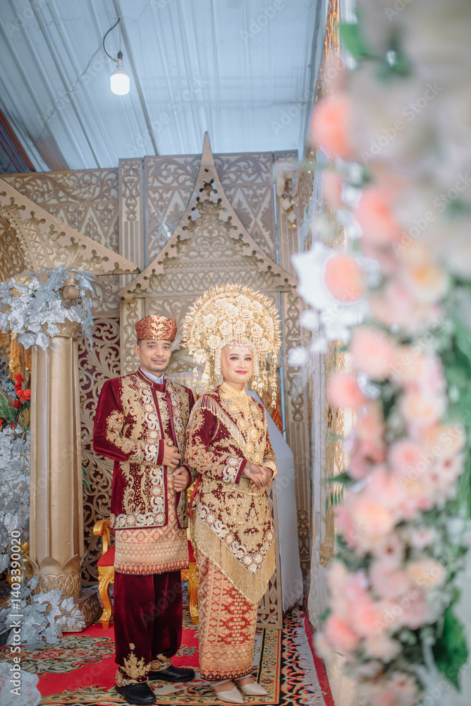 Obraz premium A wedding portrait of a Muslim couple wearing traditional Minangkabau attire from West Sumatra, featuring the iconic gold suntiang headdress.