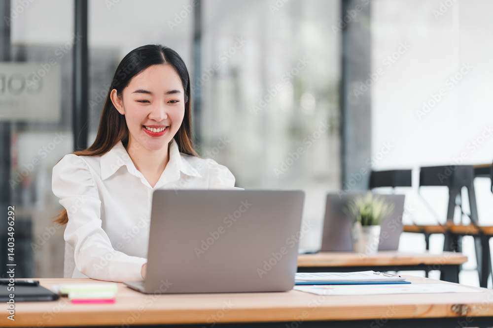 Asian businesswoman smiling while working on laptop in modern office environment, showcasing productivity and positivity Asian businesswoman smiling while working on laptop in modern office environment, showcasing productivity and positivity