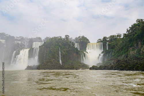 There is a beautiful waterfall located right in the center of a wide river, and it is elegantly surrounded by lush green trees