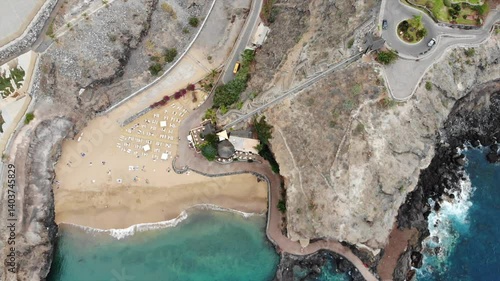 Beautiful aerial view of Tenerife, Canary islands. Tilt-up shot of turquoise ocean water, sandy beach, beautiful resort among large banana plantations, mountains in cloudy sky. 4K video footage