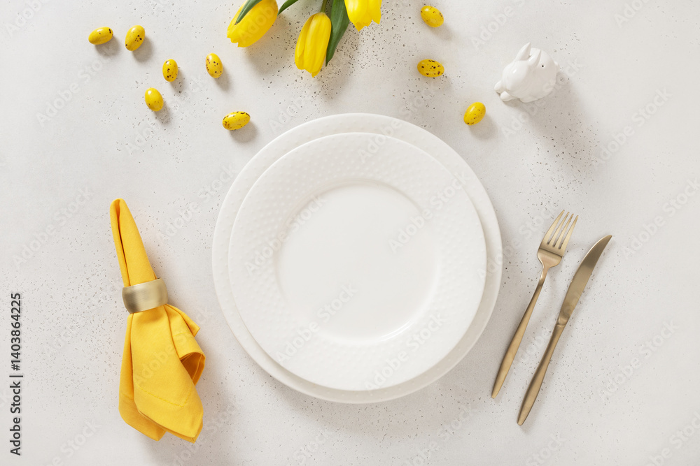 Easter table setting with spring, yellow tulips, white plates, bunny, eggs on white background. Happy Easter celebration. Copy space. View from above.