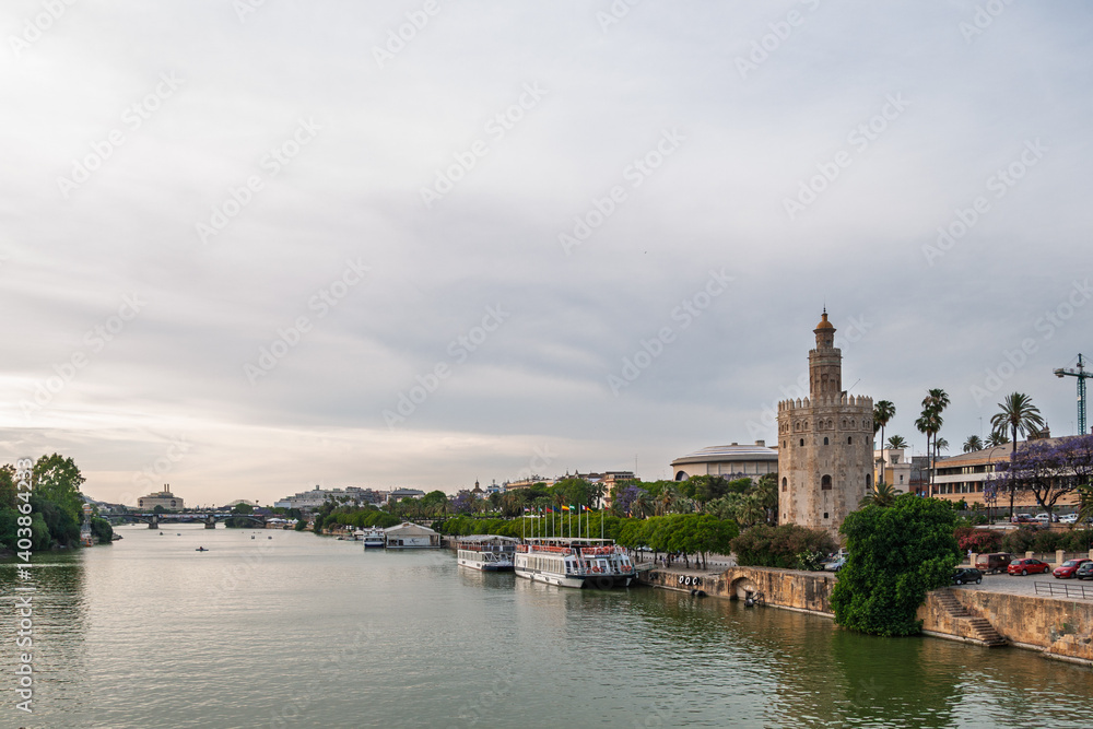Obraz premium Torre del oro reflecting on guadalquivir river with docked boats at sunset, seville, andalusia, spain