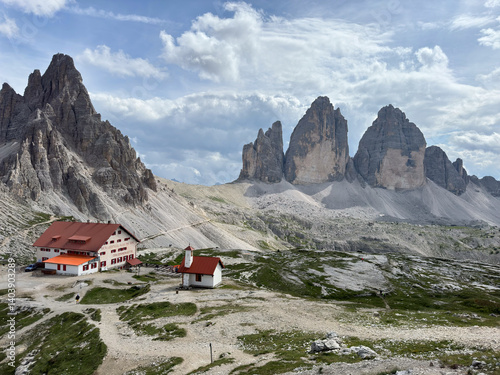 Famous mountain range Tre Cime di Lavaredo with surrounding peak monte paterno and mountain hut antonio locatelli in foredground at noon