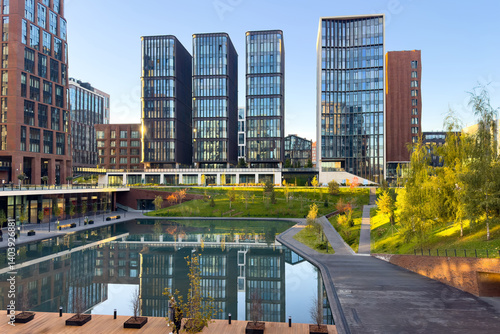 Amazing sunset view of the business class residential skyscrapers complex with green trees. The houses are reflected in the water surface of the pond. Mortgage for young families