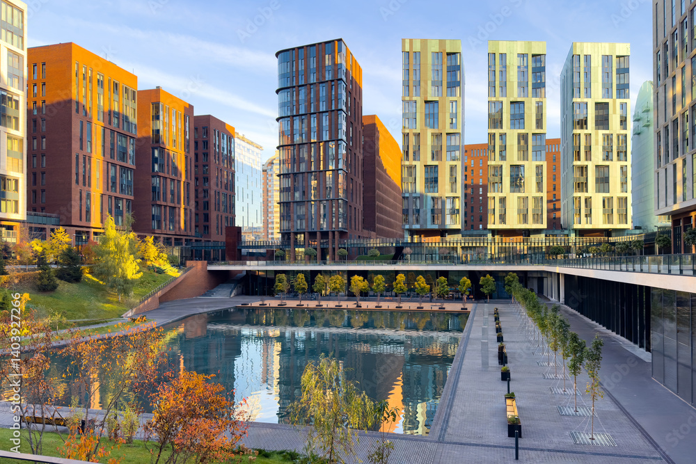 Amazing sunset view of the business class residential skyscrapers complex with green trees. The houses are reflected in the water surface of the pond. Mortgage for young families