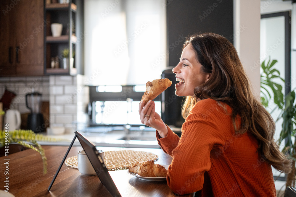 Happy woman enjoying breakfast with croissant and coffee, working remotely from home Happy woman enjoying breakfast with croissant and coffee, working remotely from home