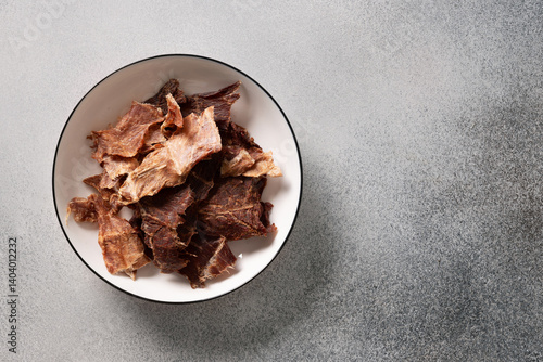 Obraz na płótnie Bowl filled with savory beef jerky on a textured gray surface. Perfect for high-protein snack ideas, exploring flavors, hiking, camping, or healthy eating themes. w salonie