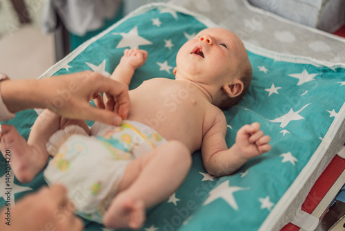 Obraz na płótnie Young mother changing her baby diaper at home. Caring mom practicing hygiene routine with newborn child. Parenthood, baby care, and early motherhood concept w salonie