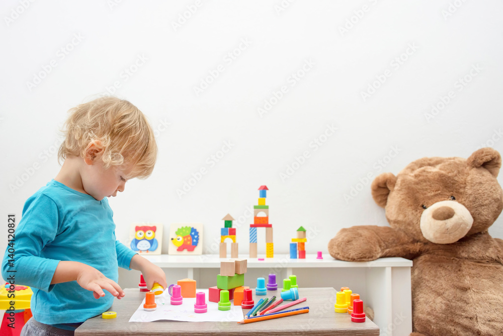 Cute little child boy having fun at home playing with colorful stamps on paper. Educational indoor activity for kids.
