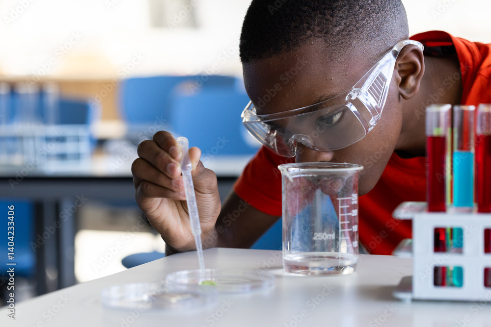 In school, boy conducting science experiment with beaker and petri dish