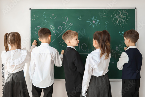 Cute little pupils drawing on blackboard in classroom, back view. School holi...