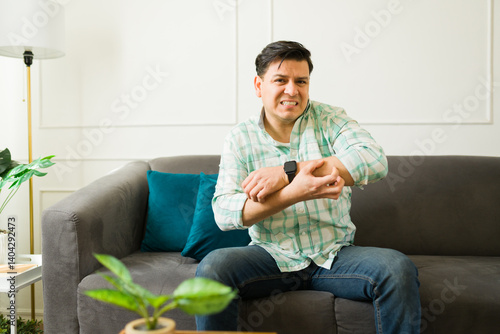 Obraz na płótnie Uncomfortable latin man scratching irritated arm with rash, experiencing allergic reaction or insect bite while resting on sofa w salonie