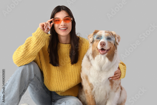 Young woman with Australian Shepherd dog in sunglasses on light background