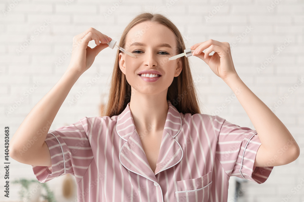 Beautiful young woman applying cosmetic oil on face with two pipettes in bathroom Beautiful young woman applying cosmetic oil on face with two pipettes in bathroom