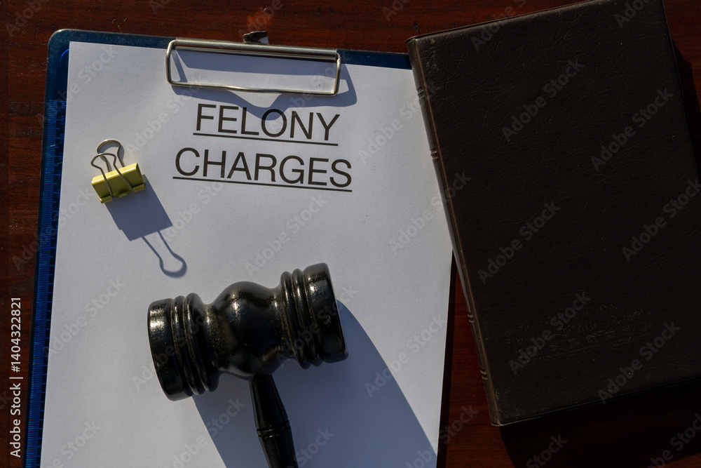 Naklejka premium A felony charges paper secured in a clipboard, placed with a gavel resting on the desk, symbolizing serious criminal offenses and judicial authority.
