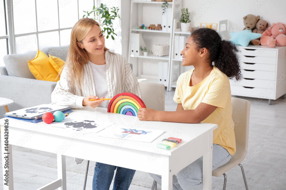 Female psychologist working with African-American girl and toy at table in office Female psychologist working with African-American girl and toy at table in office