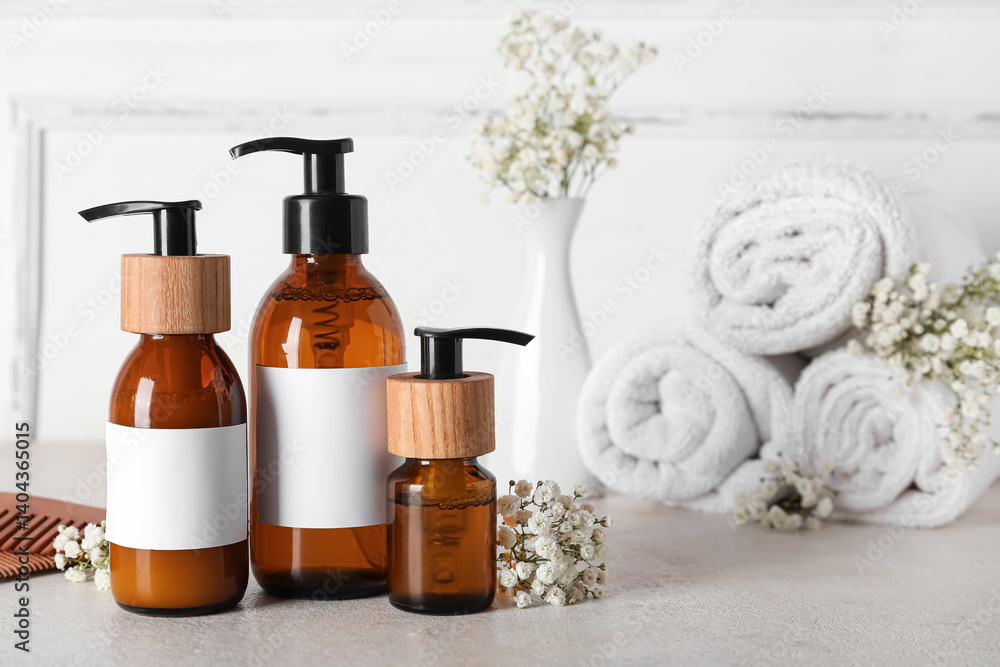 Composition with bottles of shampoo, towels and flowers on table near light wall Composition with bottles of shampoo, towels and flowers on table near light wall