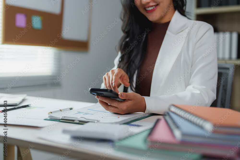 Businesswoman smiling and using smartphone while working on financial reports and business documents in modern office, managing her tasks and staying connected Businesswoman smiling and using smartphone while working on financial reports and business documents in modern office, managing her tasks and staying connected