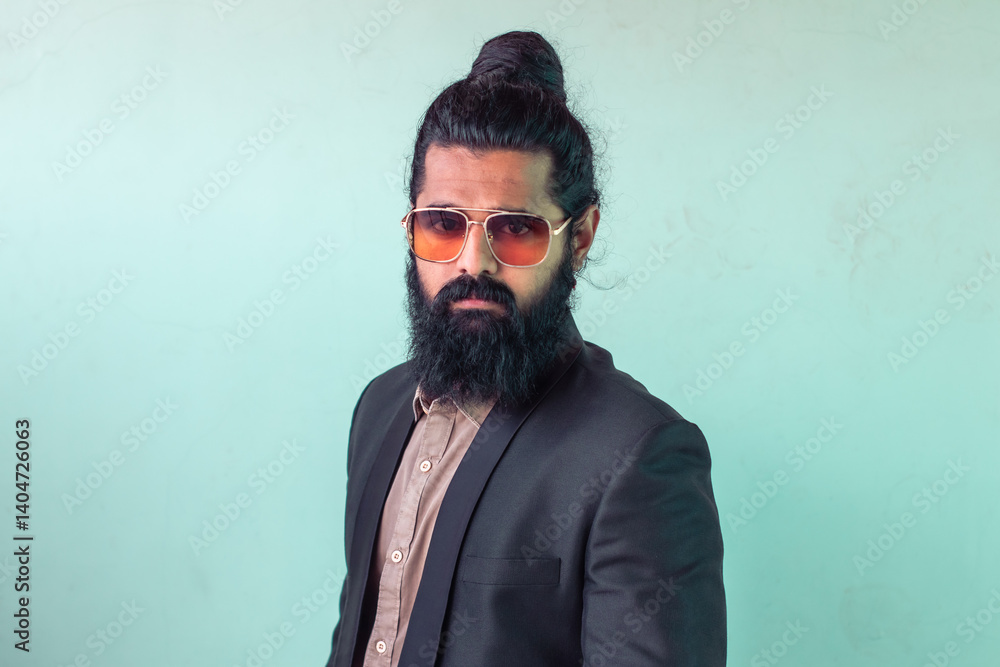 man with long dark hair tied up in topknot, full dark beard, aviator-style sunglasses. He's wearing blazer over brown shirt, posed against light teal background. expression is serious and direct man with long dark hair tied up in topknot, full dark beard, aviator-style sunglasses. He's wearing blazer over brown shirt, posed against light teal background. expression is serious and direct