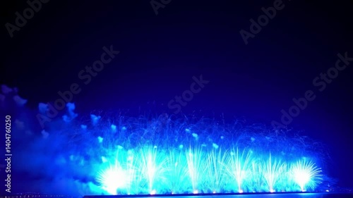 Witness the electric spectacle of brilliant blue fireworks erupting against the night sky, a dazzling cascade of shimmering sparks lighting up the lower frame in rapid succession.
