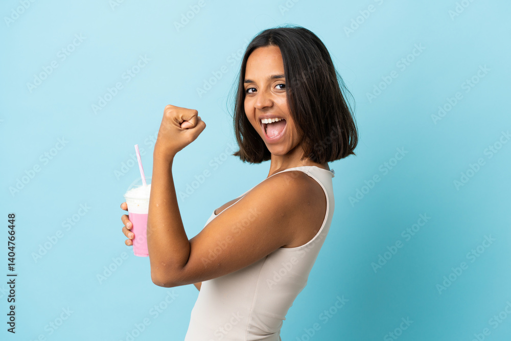 Young woman with strawberry milkshake isolated on blue background celebrating a victory Young woman with strawberry milkshake isolated on blue background celebrating a victory