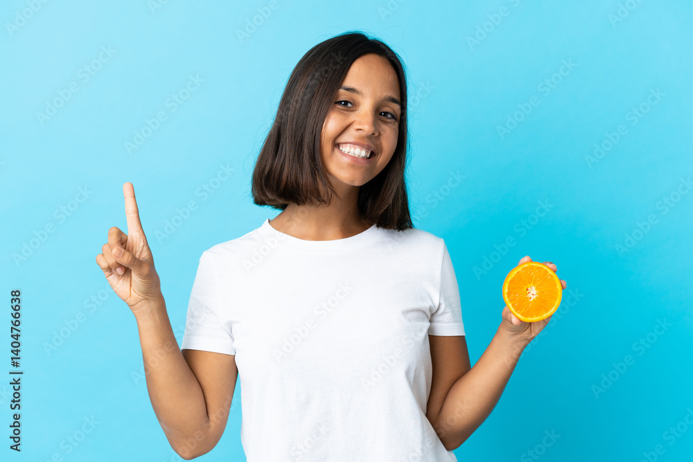 Young asian girl holding an orange isolated on blue background showing and lifting a finger in sign of the best Young asian girl holding an orange isolated on blue background showing and lifting a finger in sign of the best