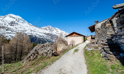 footpath crossing an alpine old village in mountainous landscape with snow-ca...