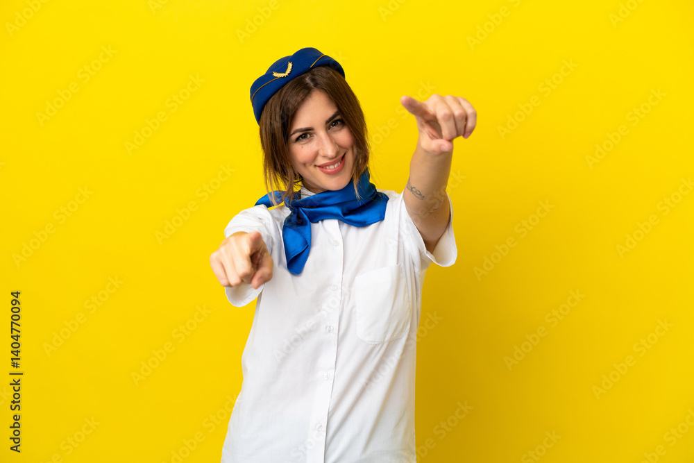 Airplane stewardess woman isolated on yellow background points finger at you while smiling Airplane stewardess woman isolated on yellow background points finger at you while smiling