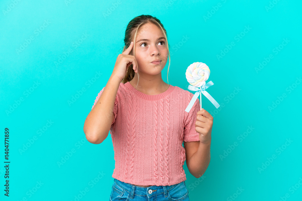 Little Caucasian girl holding a lollipop isolated on blue background having doubts and thinking Little Caucasian girl holding a lollipop isolated on blue background having doubts and thinking