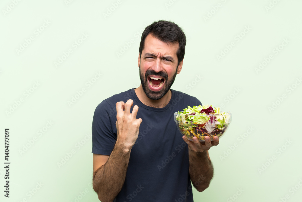 Young handsome man with salad over isolated green wall frustrated by a bad situation Young handsome man with salad over isolated green wall frustrated by a bad situation